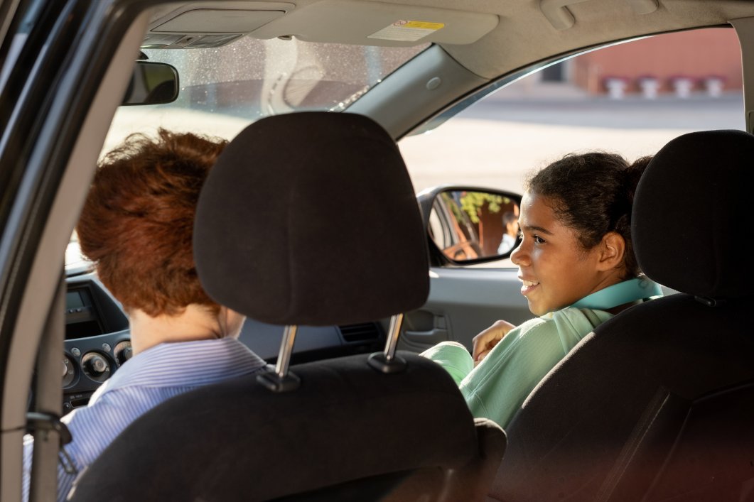 Cute youthful schoolgirl and young woman driving lessons in car on their way to school
