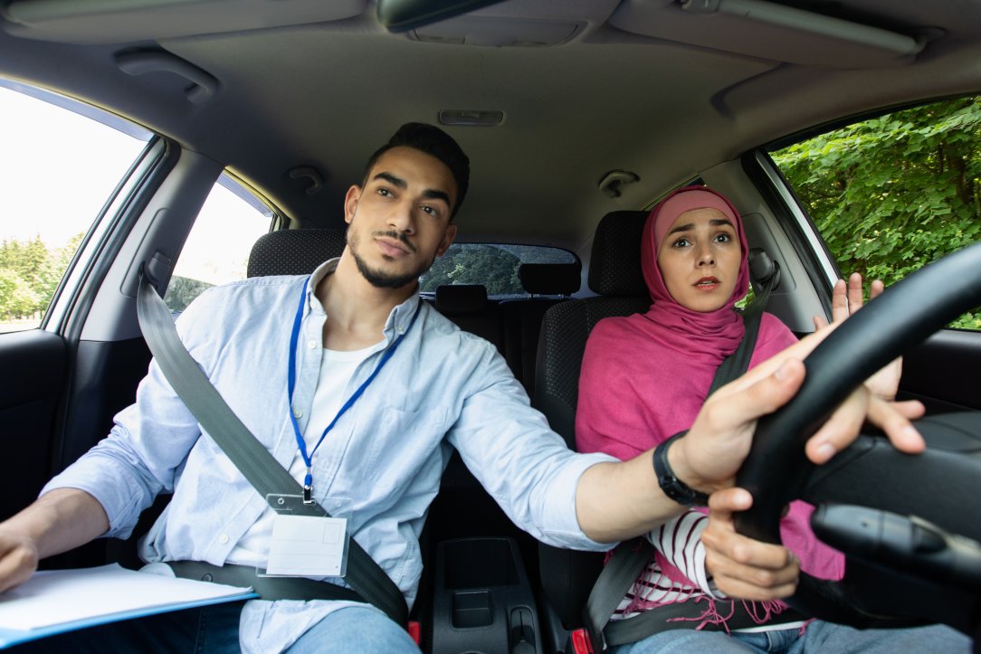Nervous Muslim Lady In Hijab Having Car Driving Lessons With Instructor, Male Teacher Helping Student To Drive Car, Holding Steering Wheel, Closeup Shot Inside Of Automobile Vehicle
