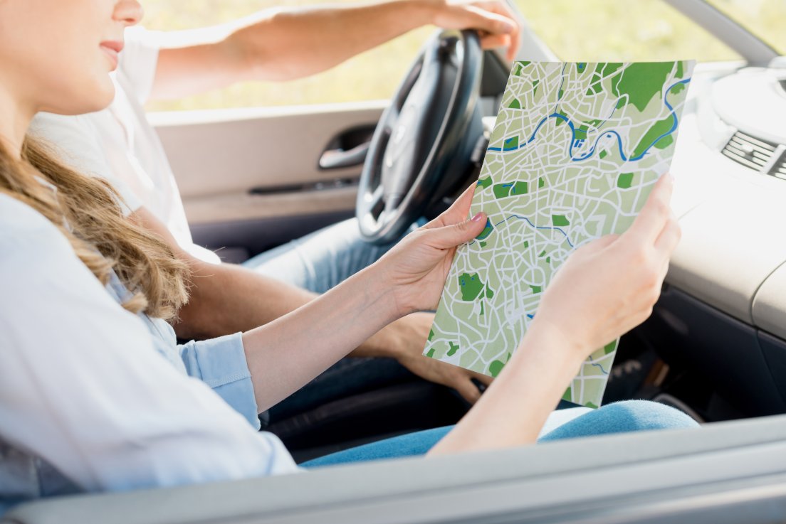Woman holding map while travelling by car with husband looking for driving lessons near me
